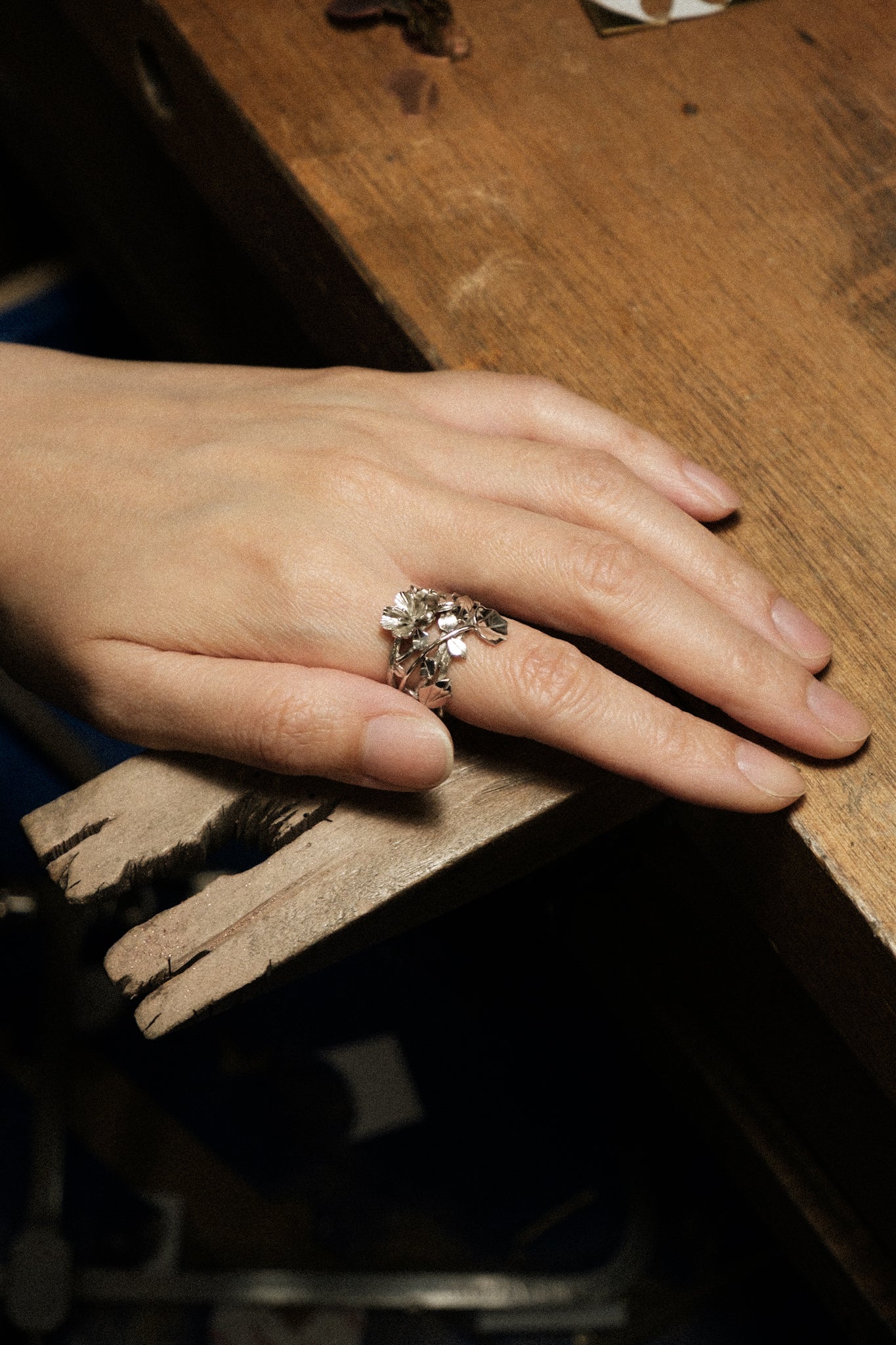 A woman’s hand lying on a jeweler’s bench with a 925 sterling silver botanical cuckoo flower design ring well fitted on her index finger.