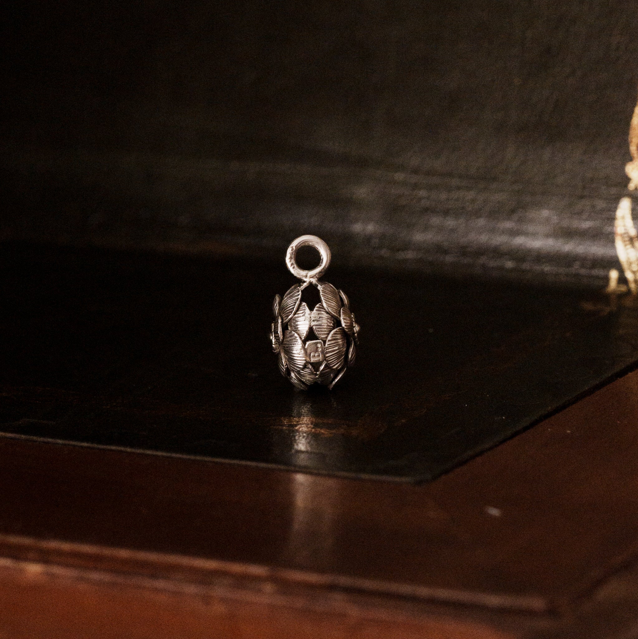 Side view of a 925 sterling silver camellia flower-shaped pendant on a dark wooden surface
