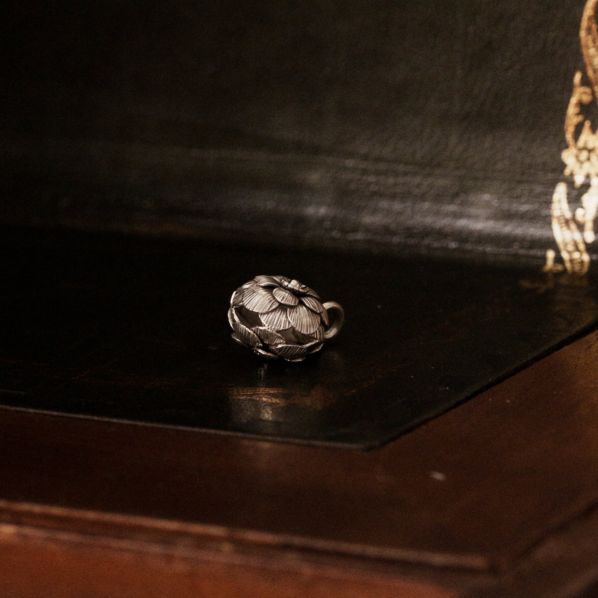 a 925 sterling silver camellia flower-shaped pendant lying down on a dark wooden surface, revealing the hollow design as a bell