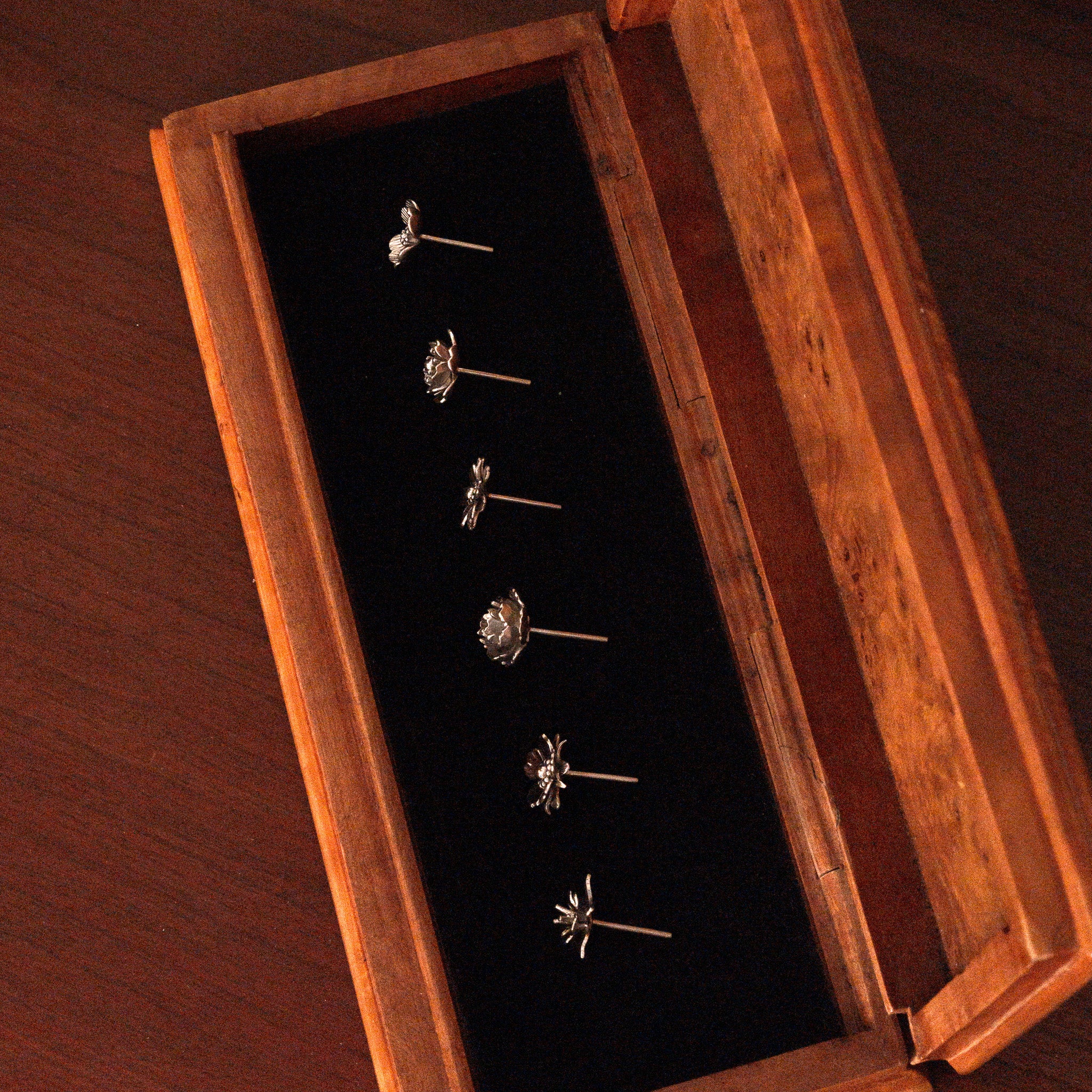 A full set of sterling silver ear studs in floral design displaying on a wooden jewelry case