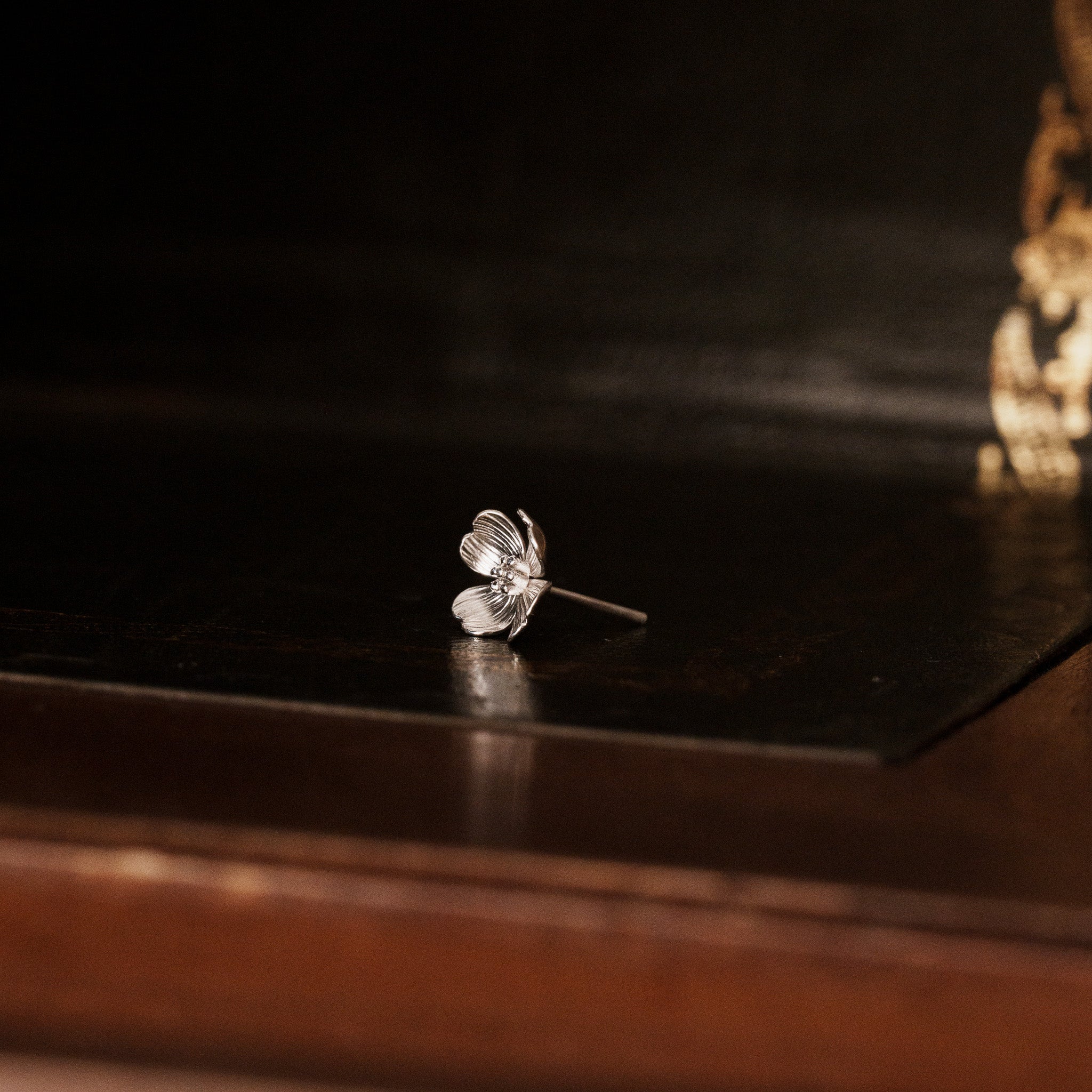side view of a 925 sterling silver dogwood flower shaped earring on a vintage dark wooden trunk