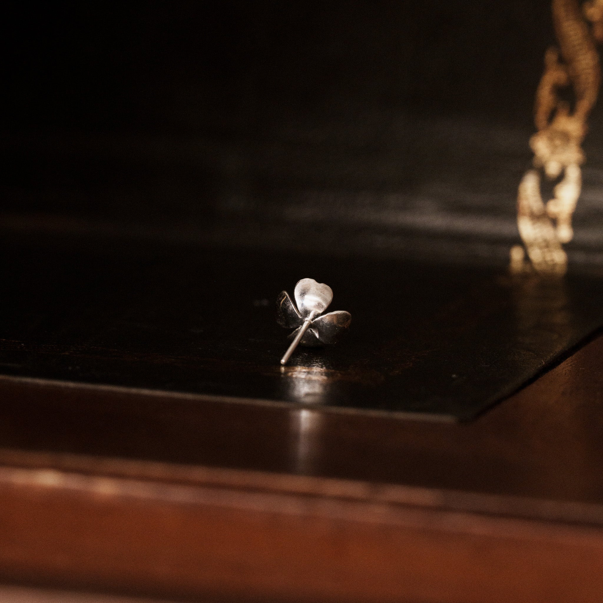 back view of a 925 sterling silver dogwood flower shaped earring on a vintage dark wooden trunk