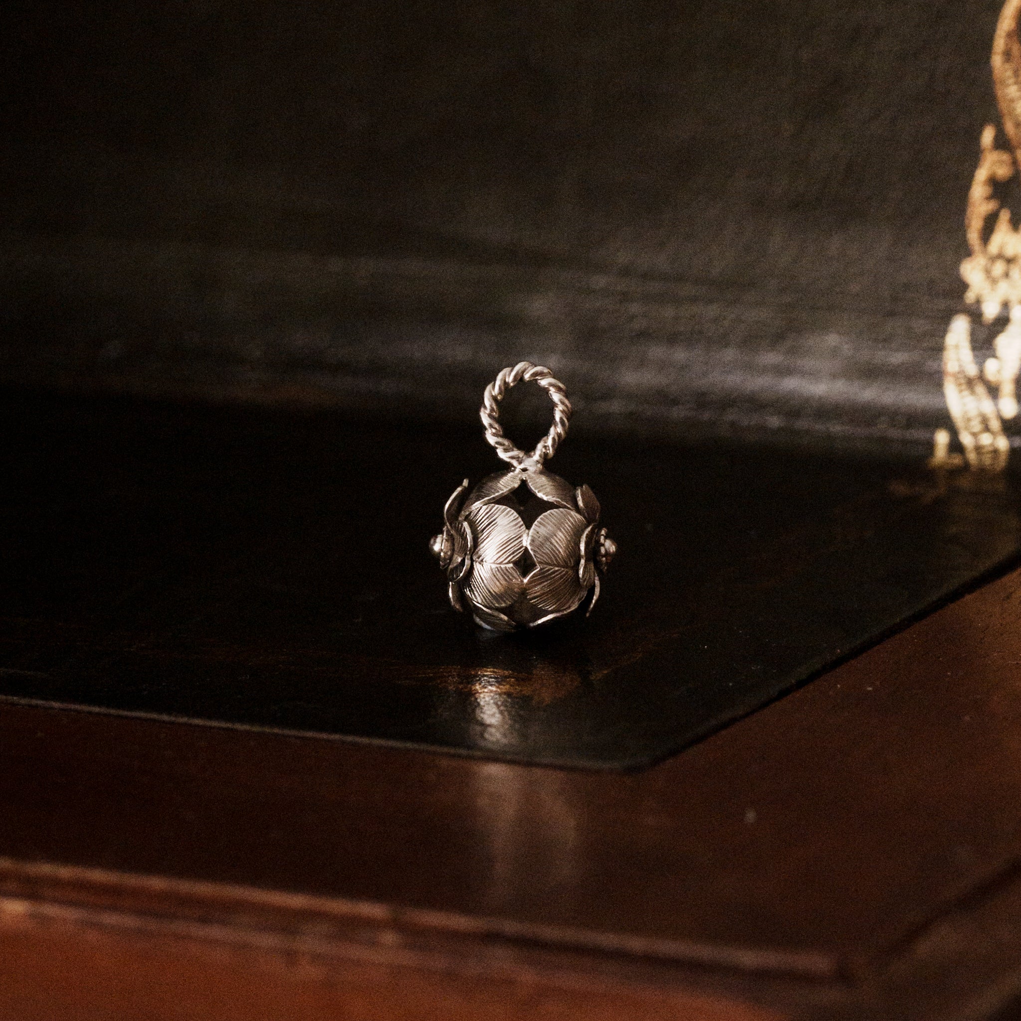 Side view of a 925 sterling silver four leaf clover shaped pendant on a dark wooden surface