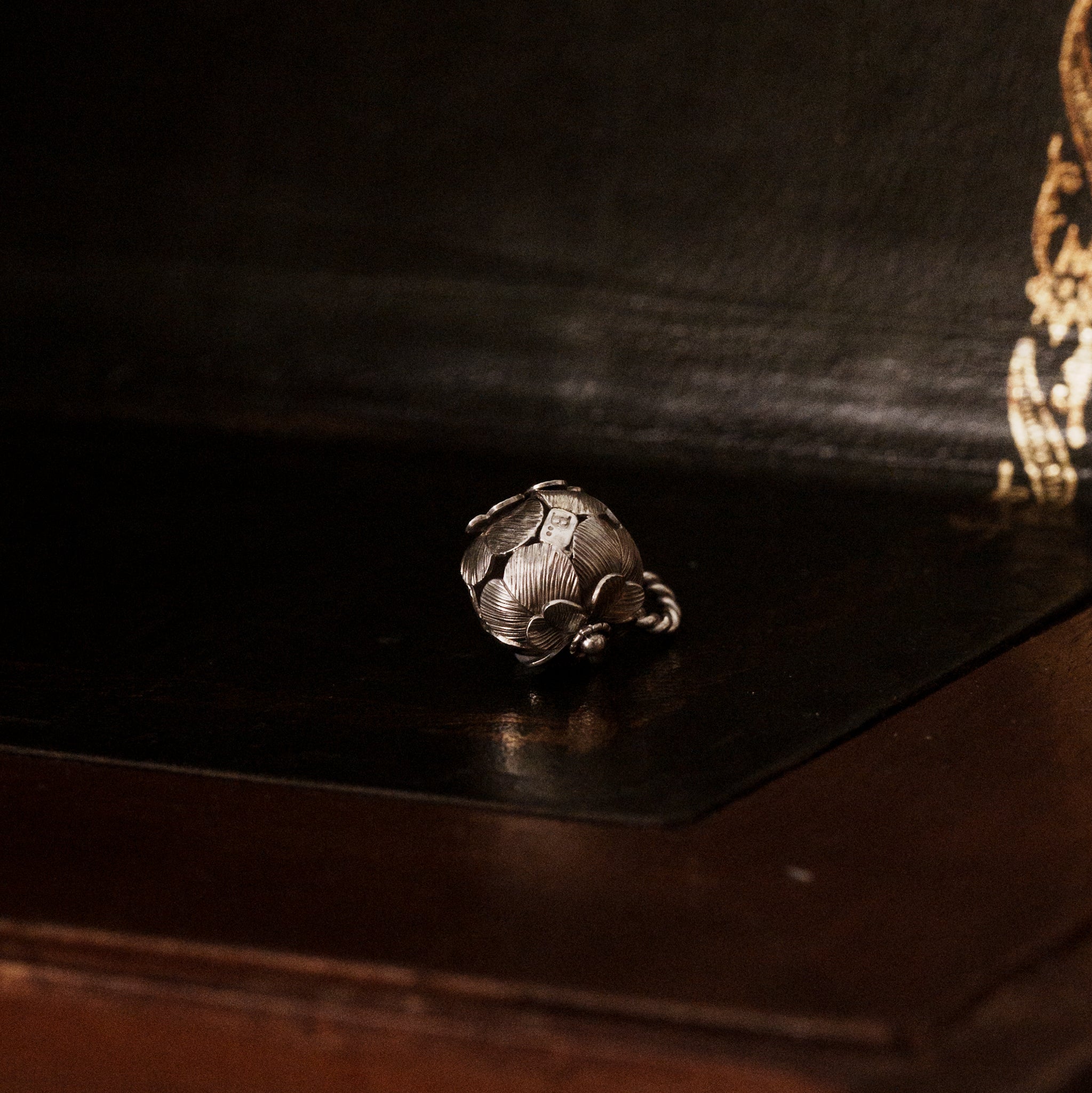 a 925 sterling silver four leaf clover shaped pendant lying down on a dark wooden surface, showing the brand's logo tag with leaf details