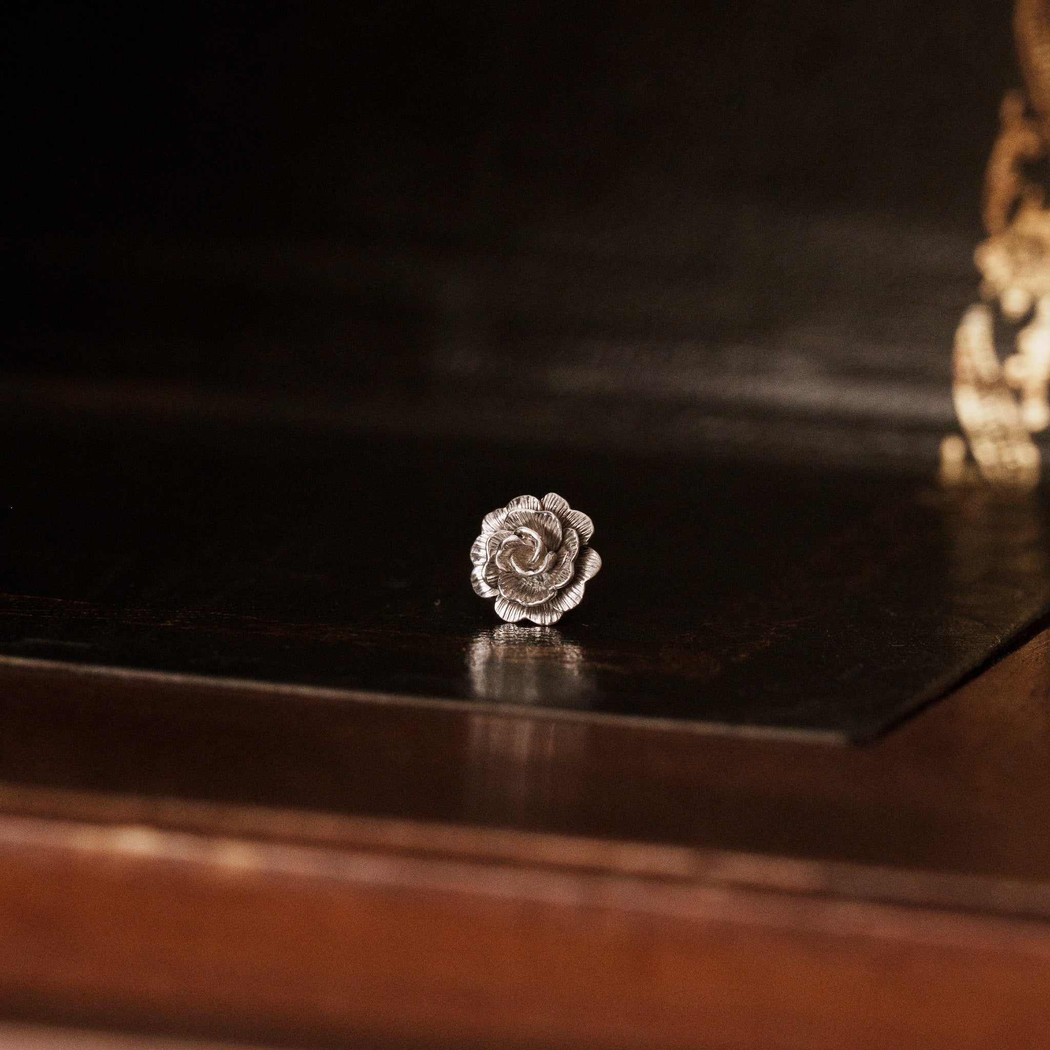 Front view of 925 sterling silver rose flower shaped earring on a vintage dark wooden trunk