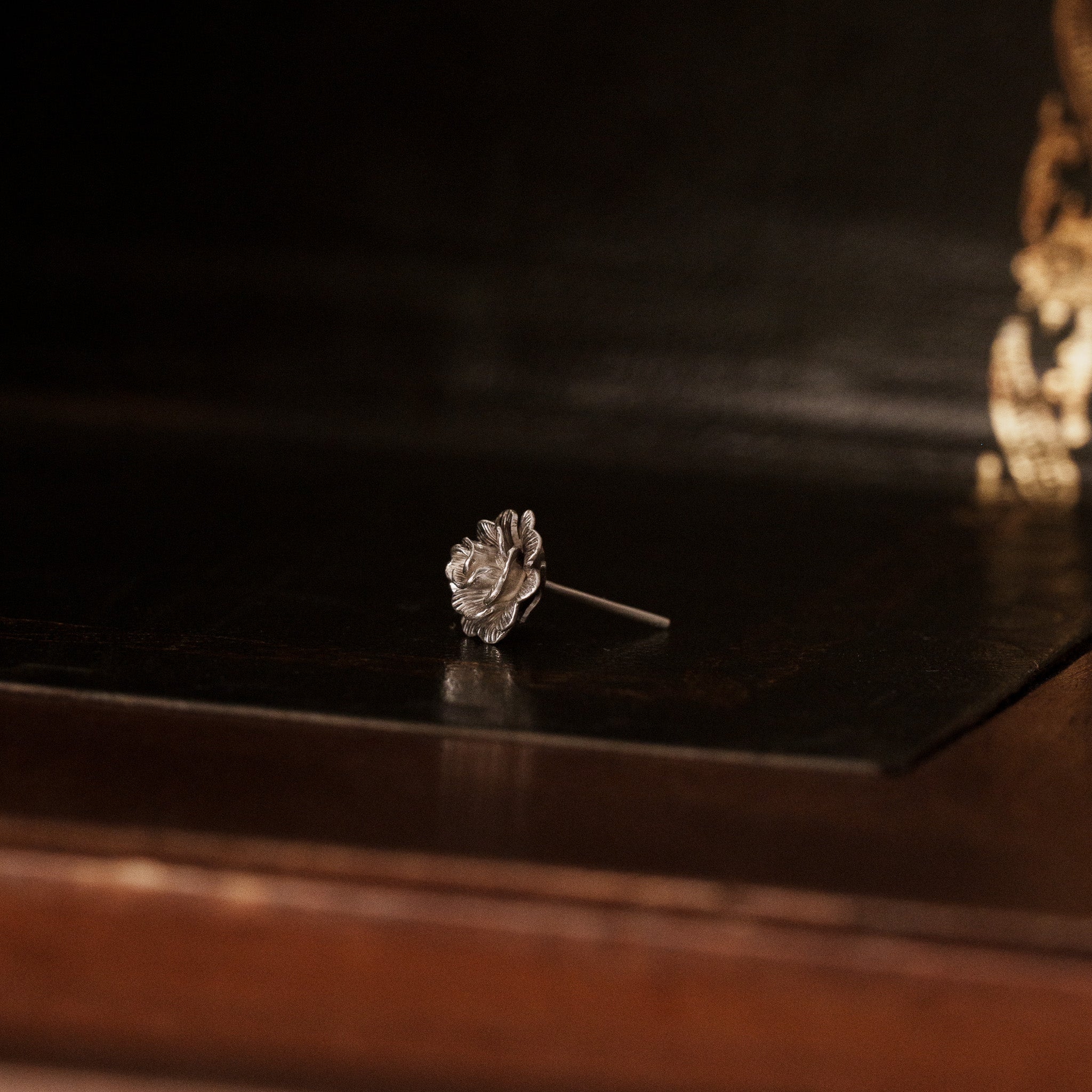 side view of a 925 sterling silver rose flower shaped earring on a vintage dark wooden trunk, show the ear pin
