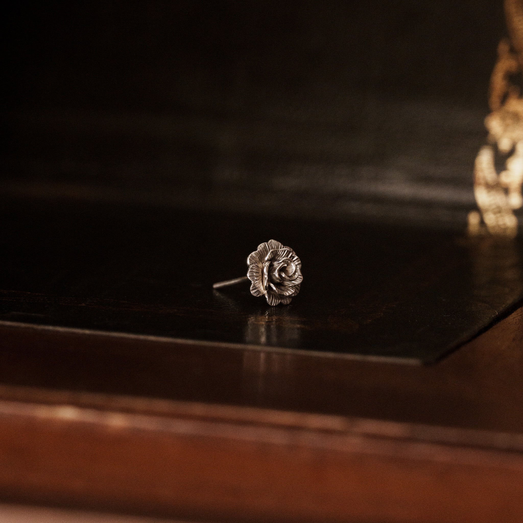 side view of a 925 sterling silver rose flower shaped earring on a vintage dark wooden trunk