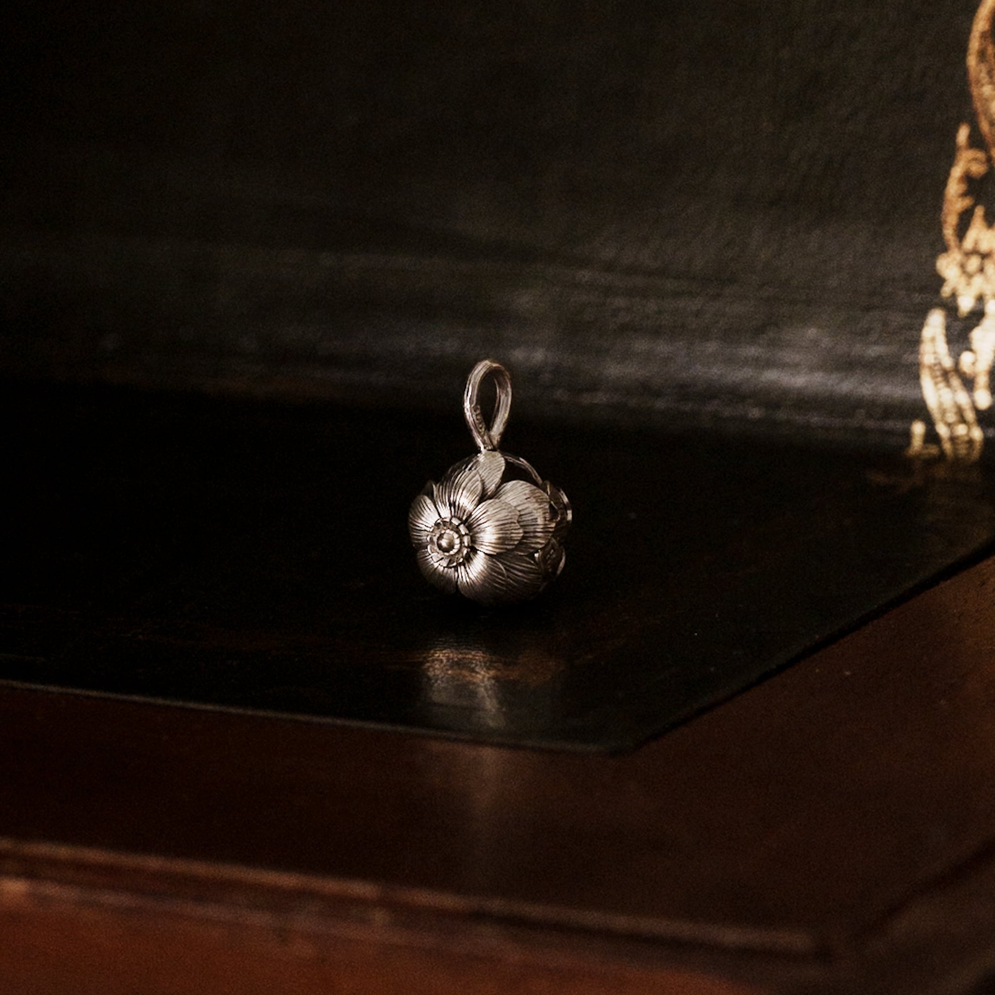 925 sterling silver sakura flower-shaped pendant on a dark wooden surface, showing detailed layers of flower petals