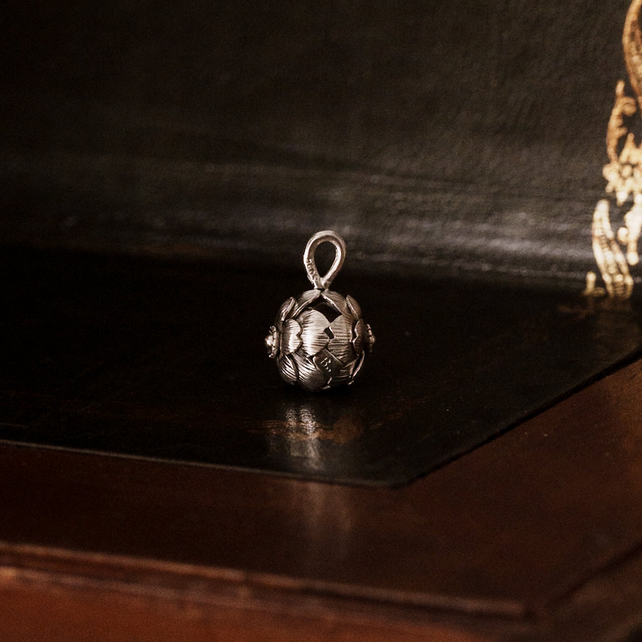 Side view of a 925 sterling silver sakura flower-shaped pendant on a dark wooden surface, showing the brand's logo tag