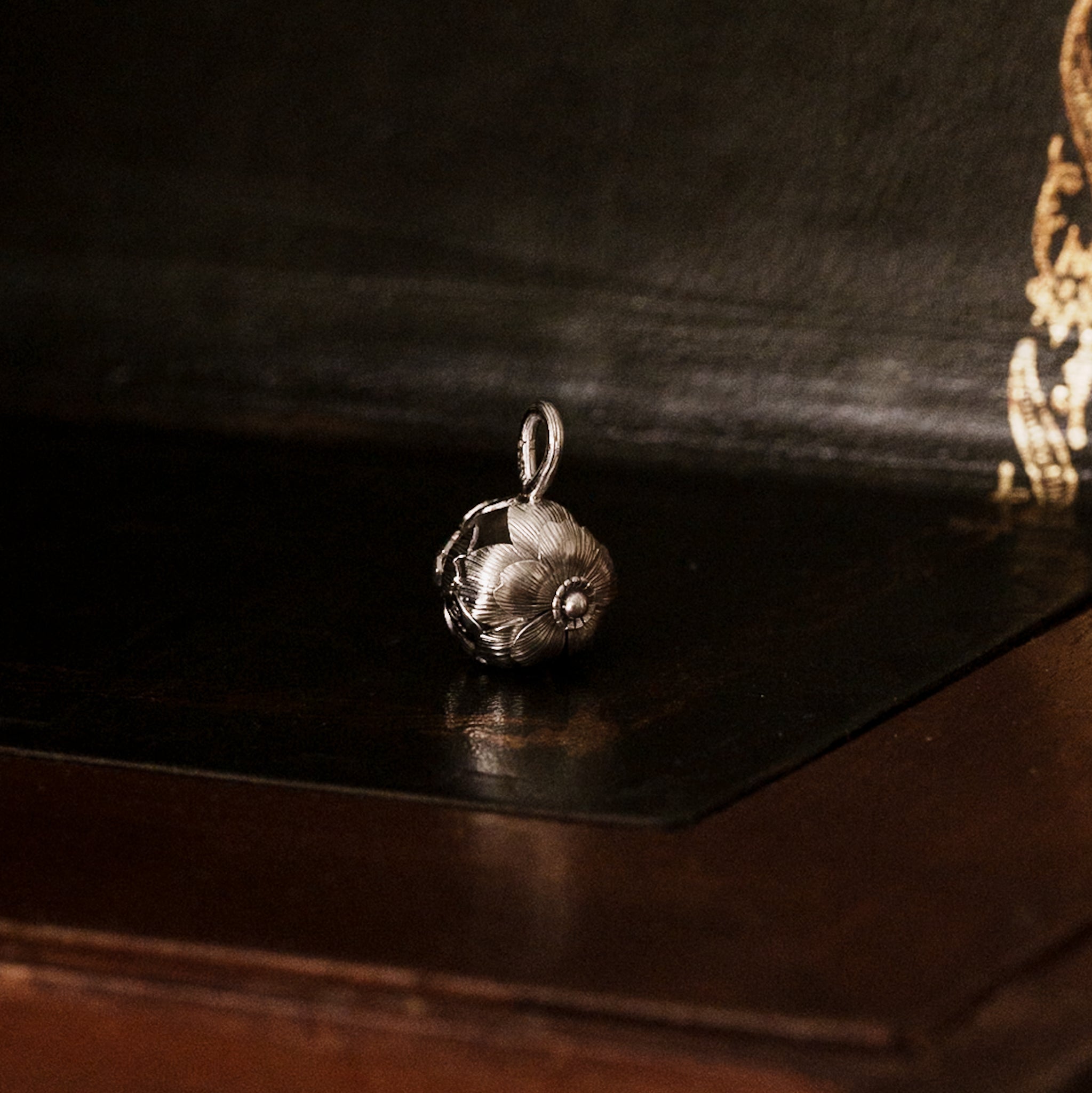 Side view of a 925 sterling silver sakura flower-shaped pendant on a dark wooden surface